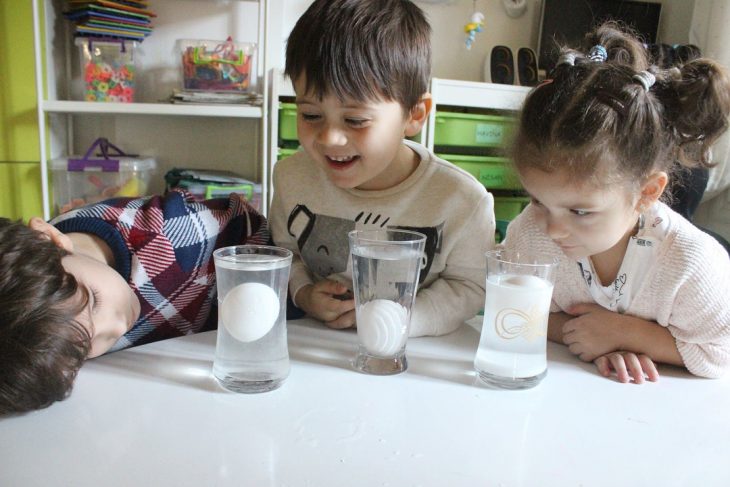 Ni&ntilde;os mirando un experimento en frascos con huevos.